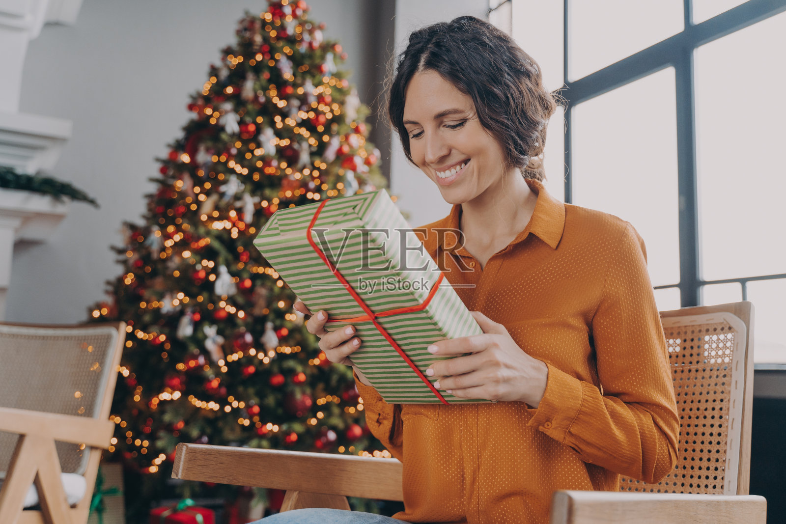 美丽快乐的意大利女人坐在家里装饰节日的圣诞树旁,手里拿着礼物照片摄影图片