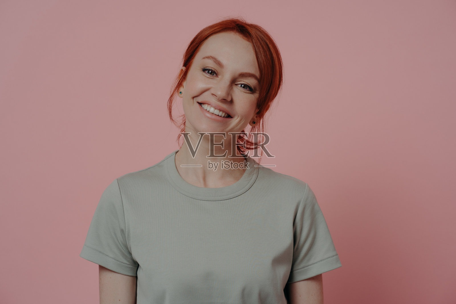 积极放松的红发女人,外表愉快,微笑着,孤立在粉红色上照片摄影图片