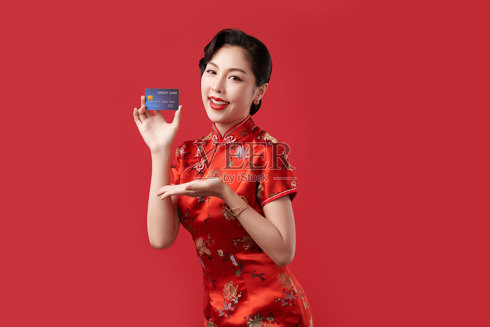 中国新年快乐,美丽的年轻亚洲女子穿着传统的旗袍旗袍拿着红色背景的信用卡,照片摄影图片