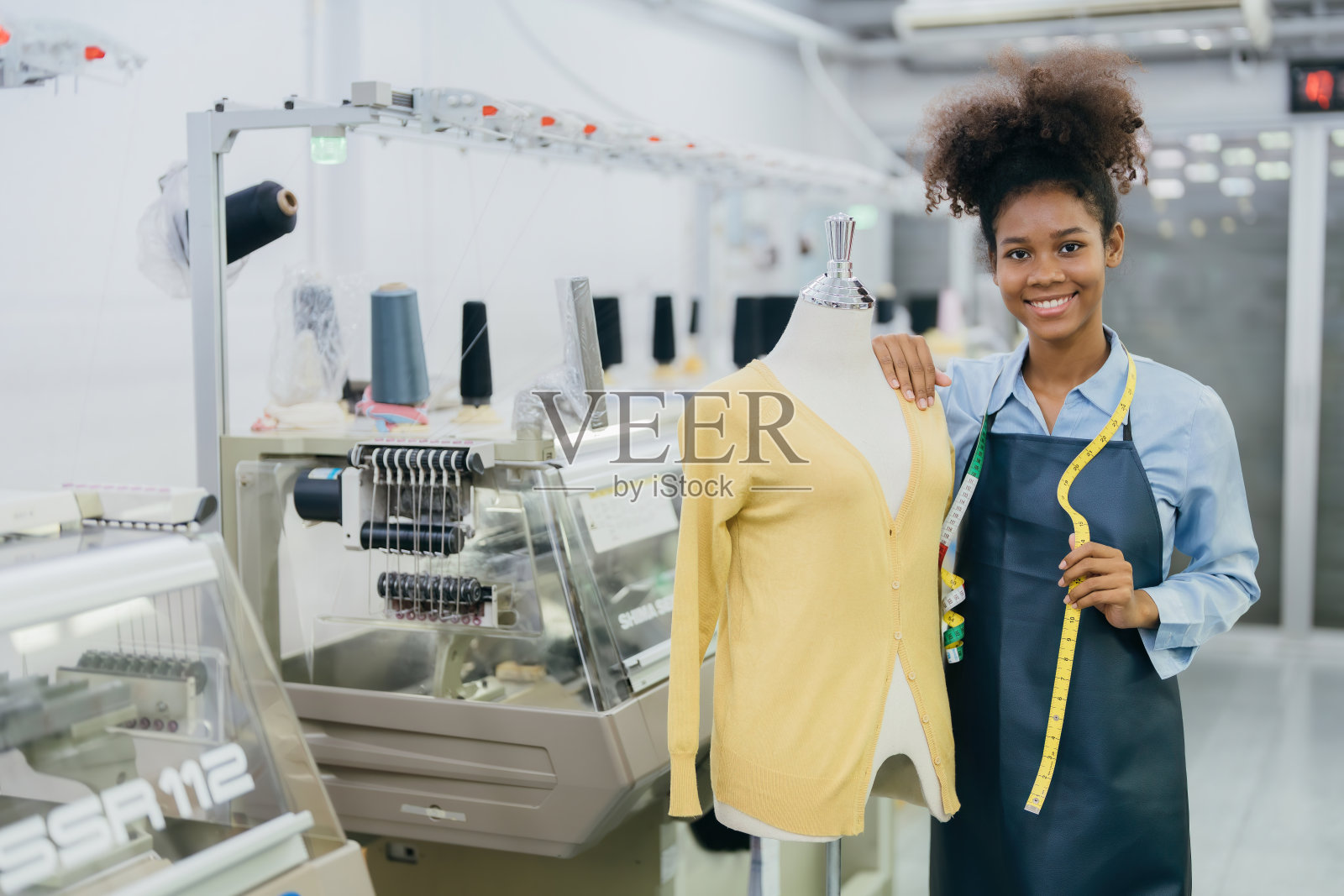 美国女设计师一位女裁缝站在一个人体模型旁边,手里拿着她设计的衣服和卷尺。附近有一台缝纫机在工作。照片摄影图片