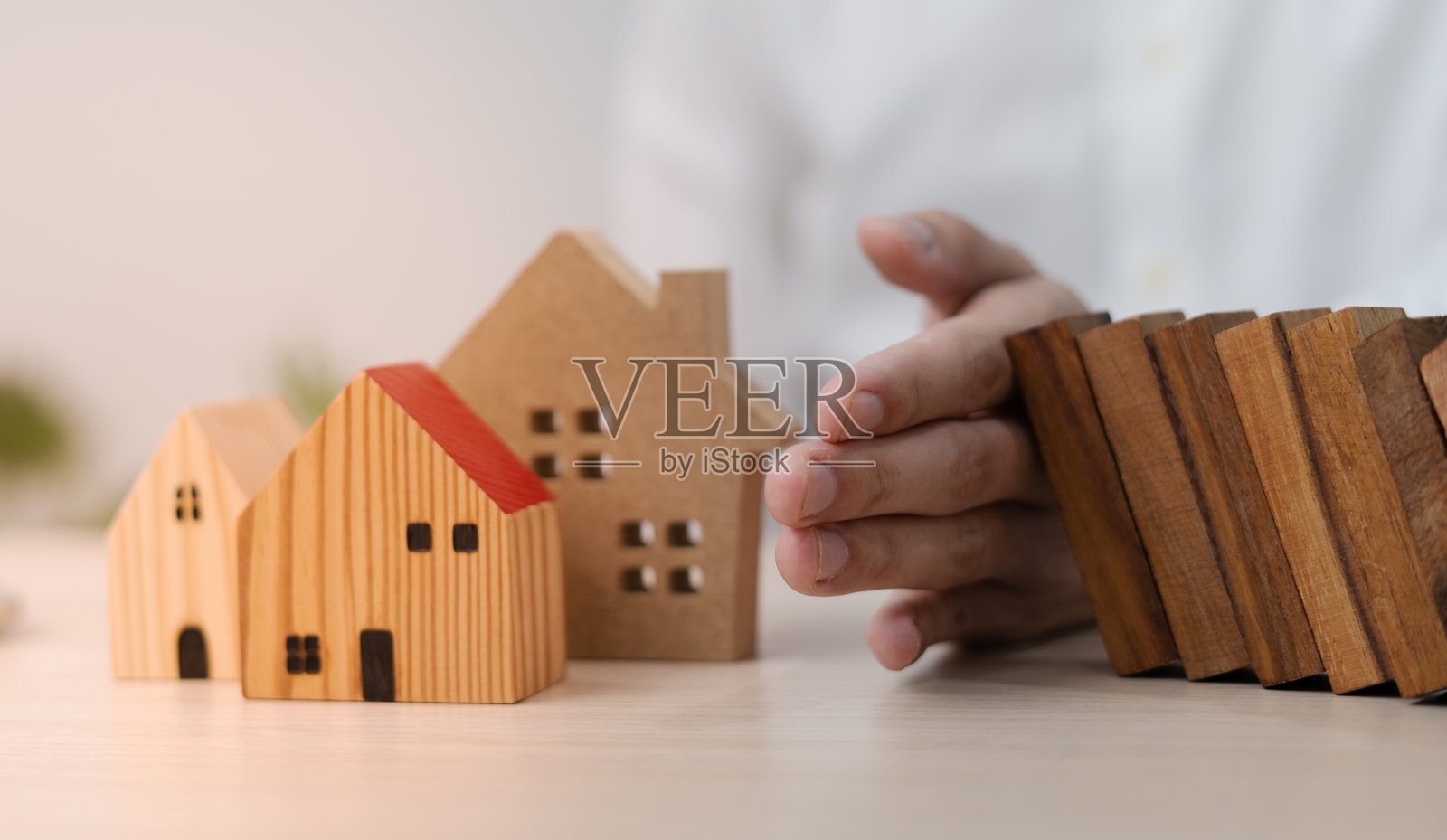 用手保险保护房子。木制的多米诺骨牌就要倒在房子上了。家庭保险或房屋保险的概念照片摄影图片