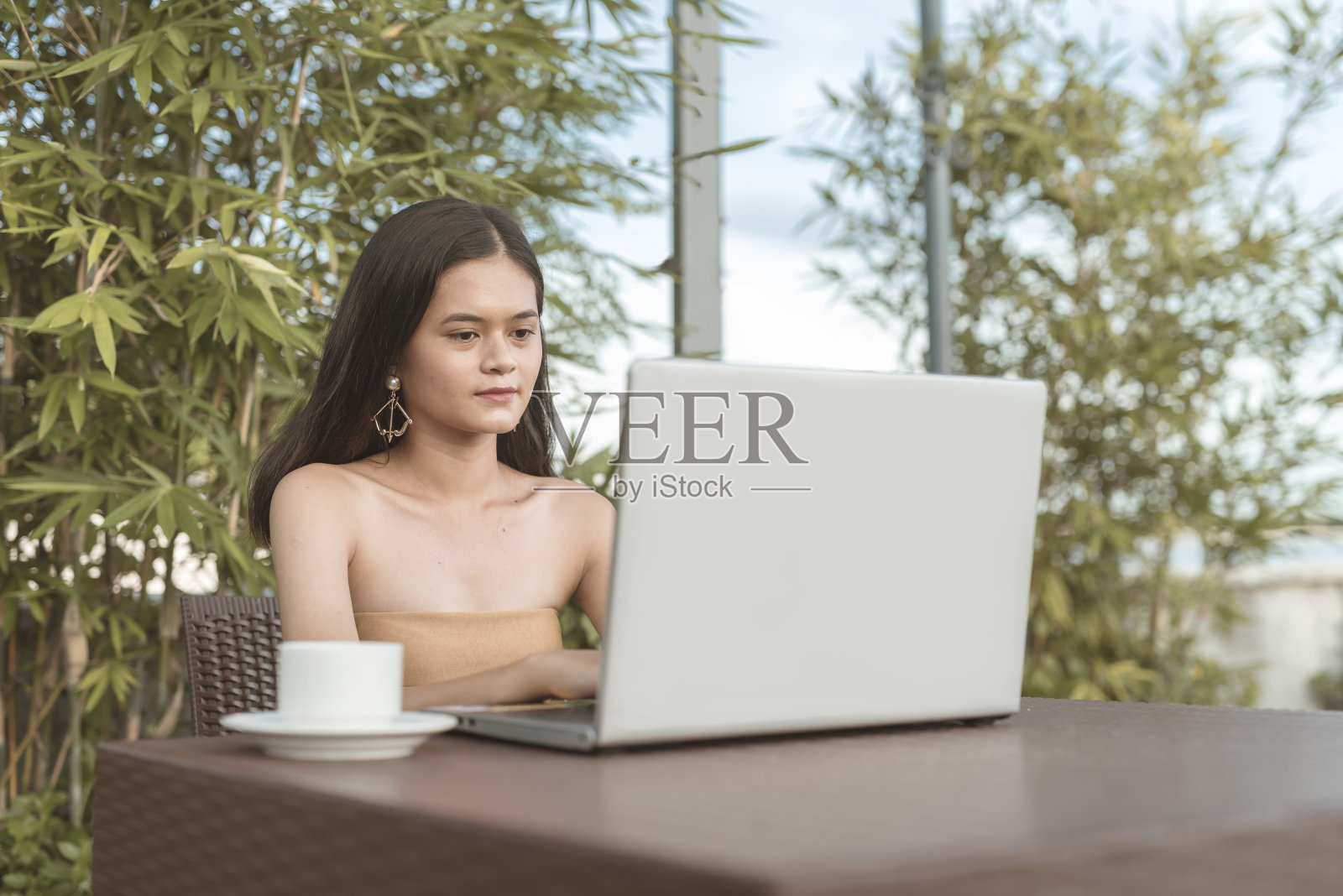 一个欧洲和亚洲混血的年轻女子在笔记本电脑上打字。穿着无袖上衣。照片摄影图片
