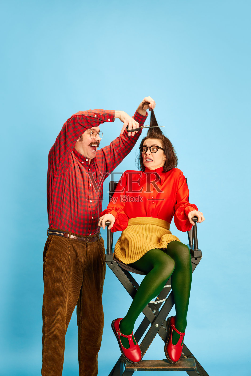 肖像与害怕的女人和疯狂的理发师做新的发型在蓝色的工作室背景。糟糕的理发师照片摄影图片