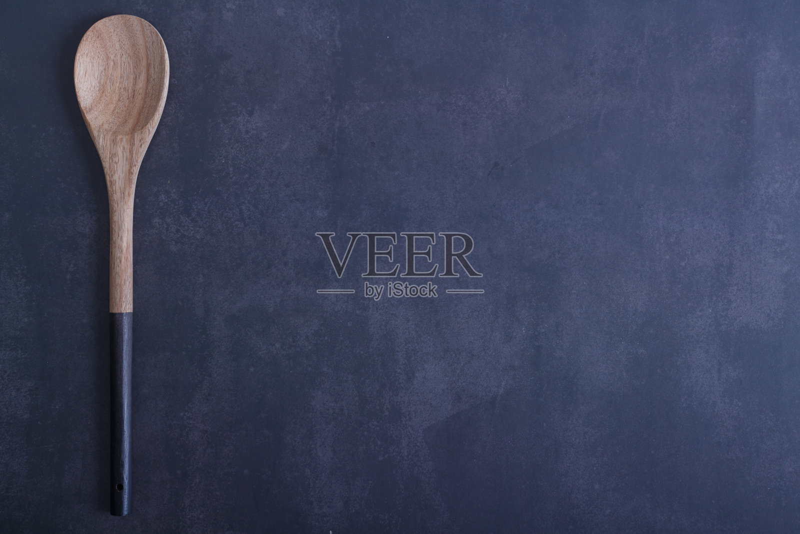 Wooden spoon with black handle on a blue dark background.照片摄影图片