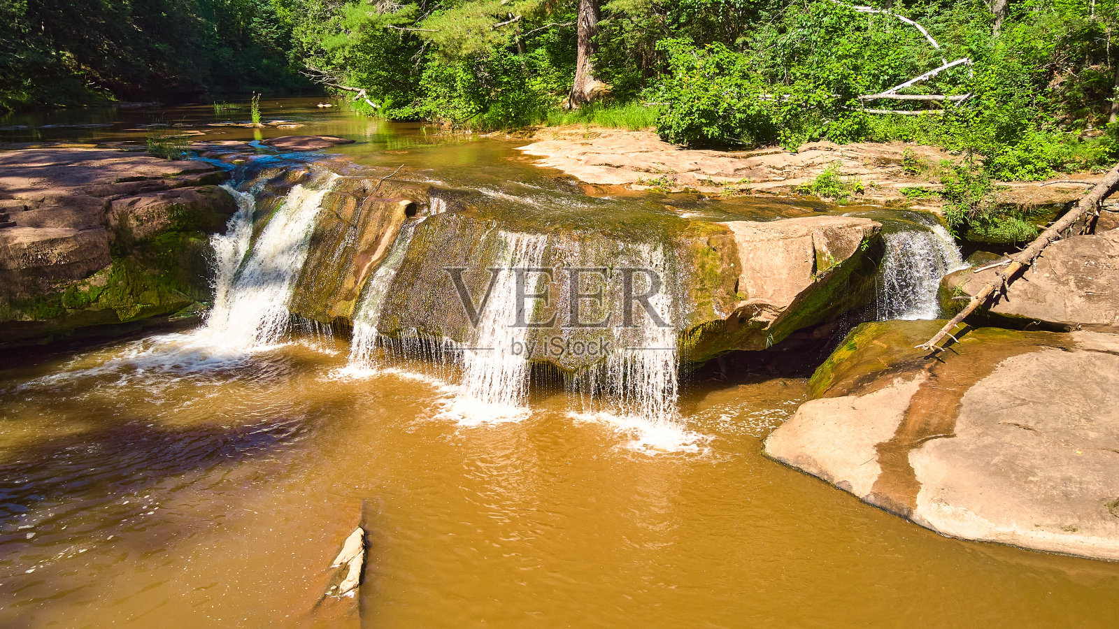 Close view of waterfall over large boulder with brown water照片摄影图片