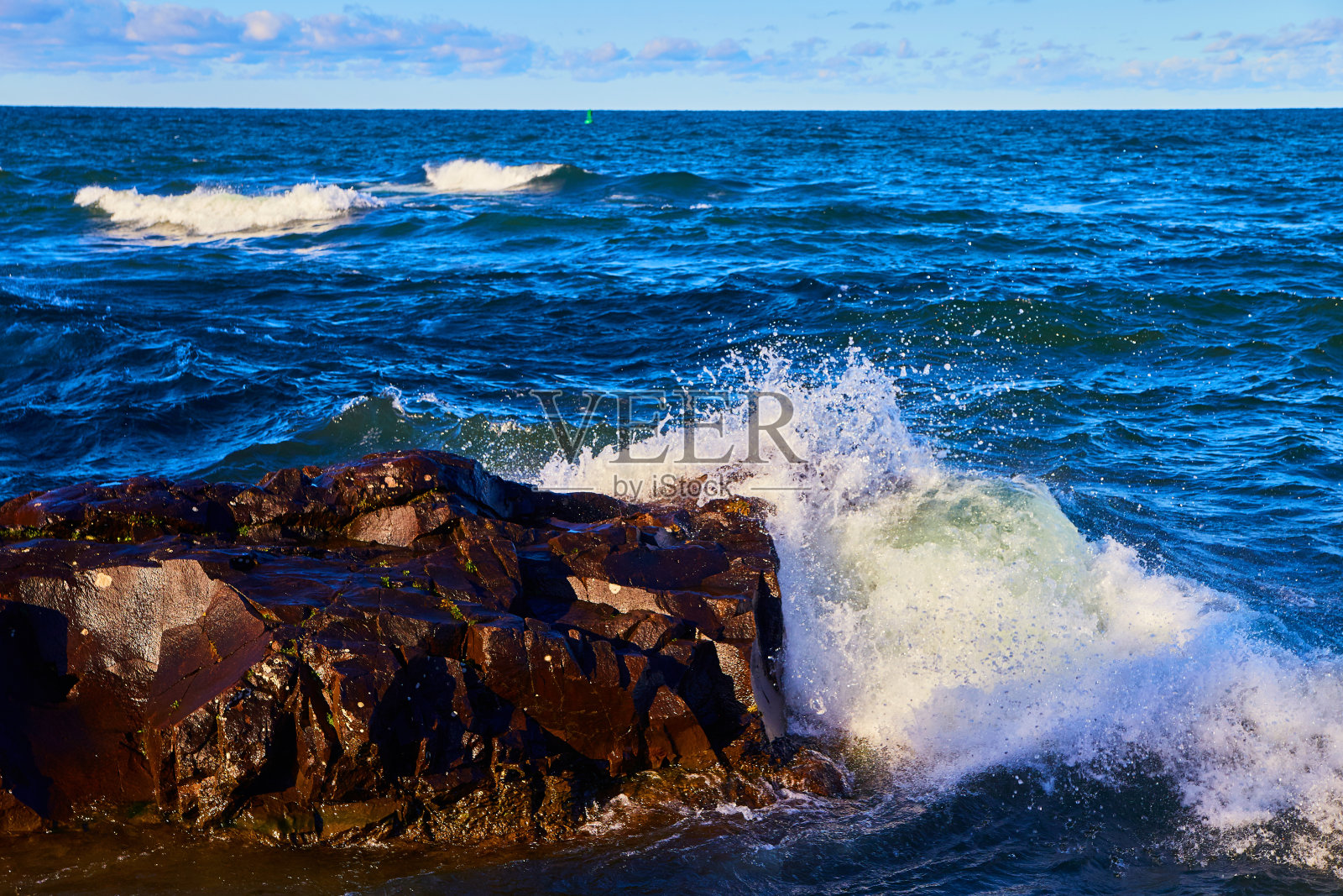 经典的岩石与浪花的冲击和远处的绿色帆船照片摄影图片