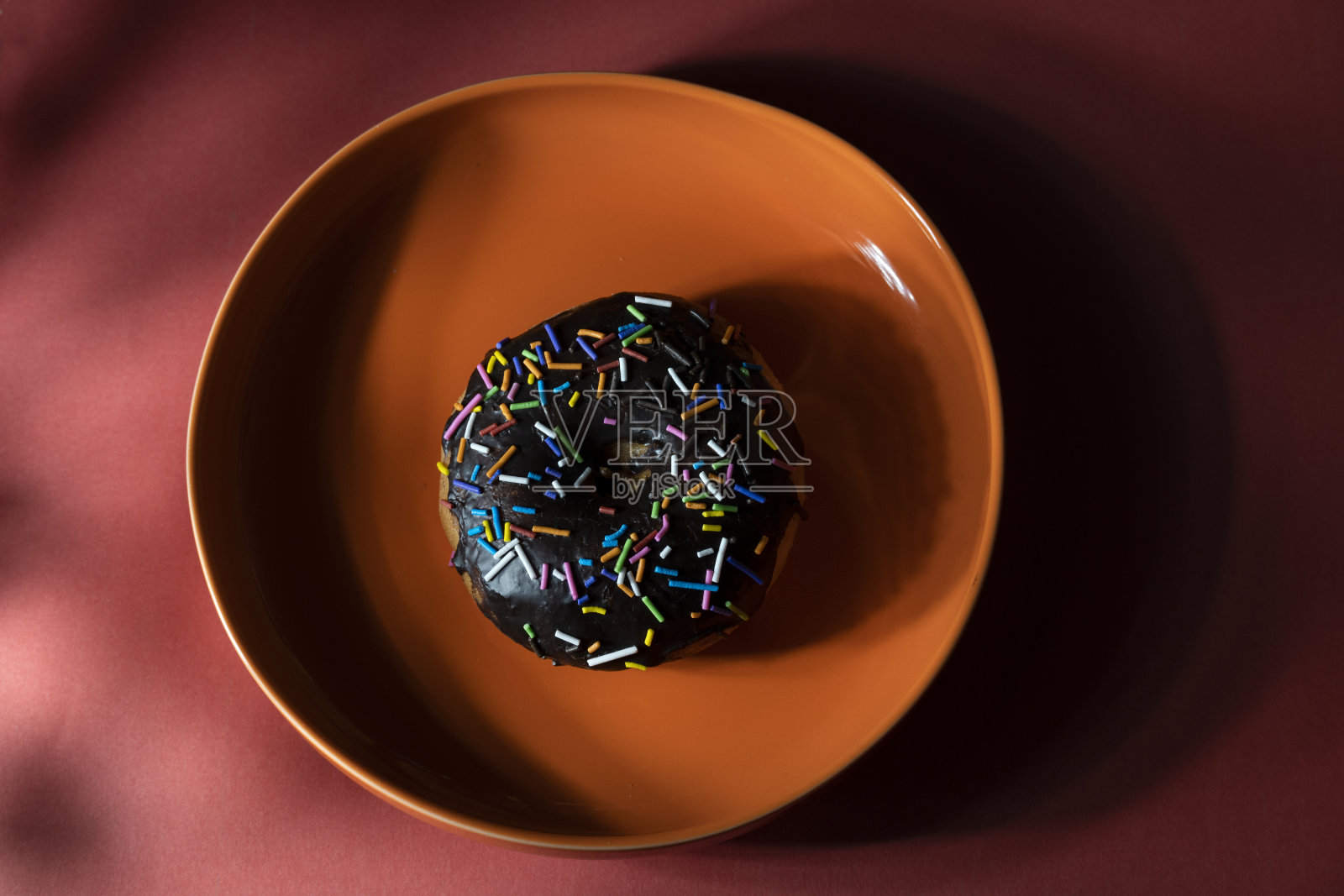 色彩缤纷的甜甜圈在橙色盘子上的红色背景。俯视图照片摄影图片