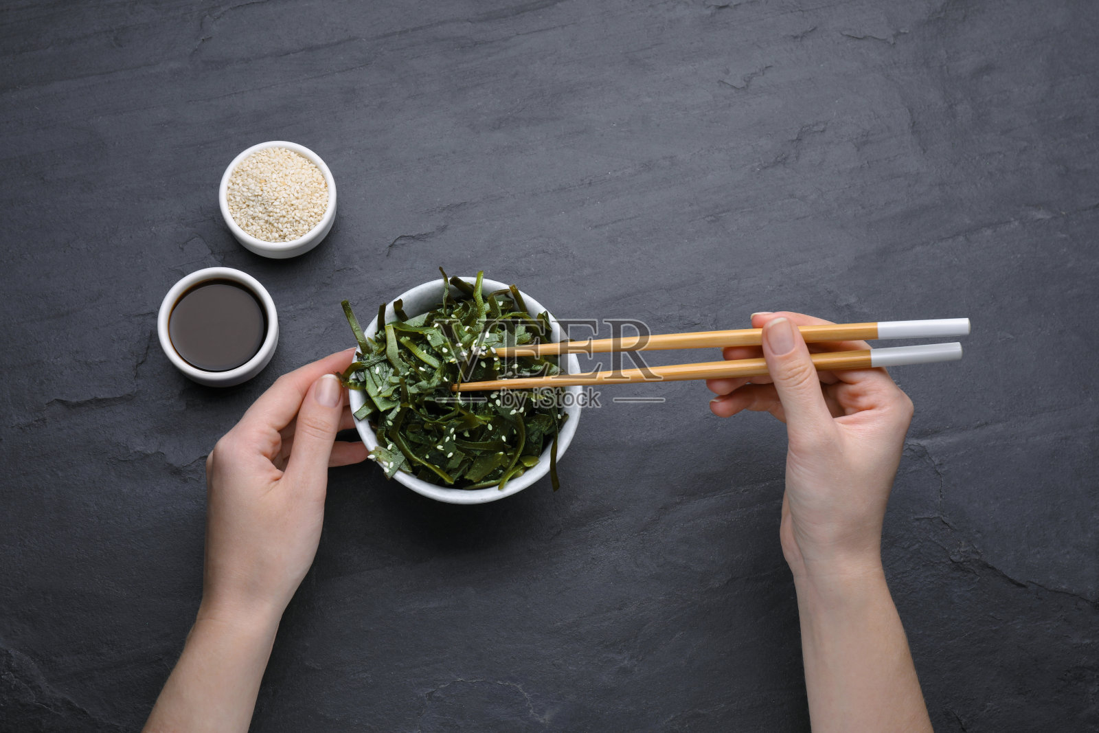女人在黑色的桌子上吃新鲜的海带(海带),俯视图照片摄影图片