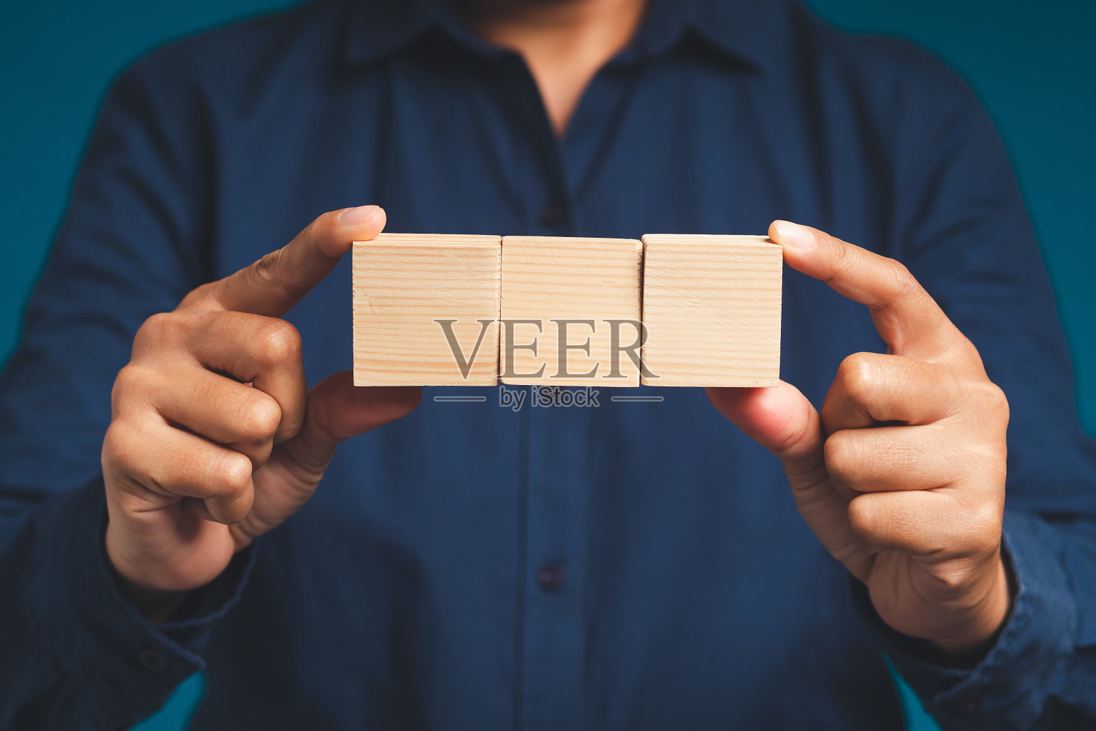 一个商人的手拿着三个空白的木立方体,站在蓝色背景上。照片摄影图片