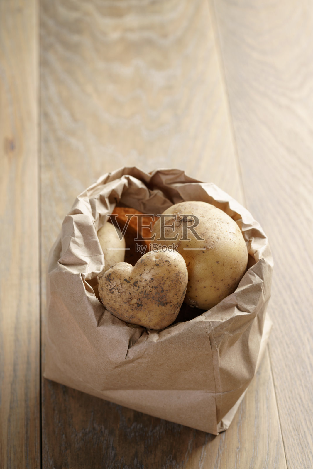 橡木桌子上的牛皮纸袋里的新鲜土豆照片摄影图片