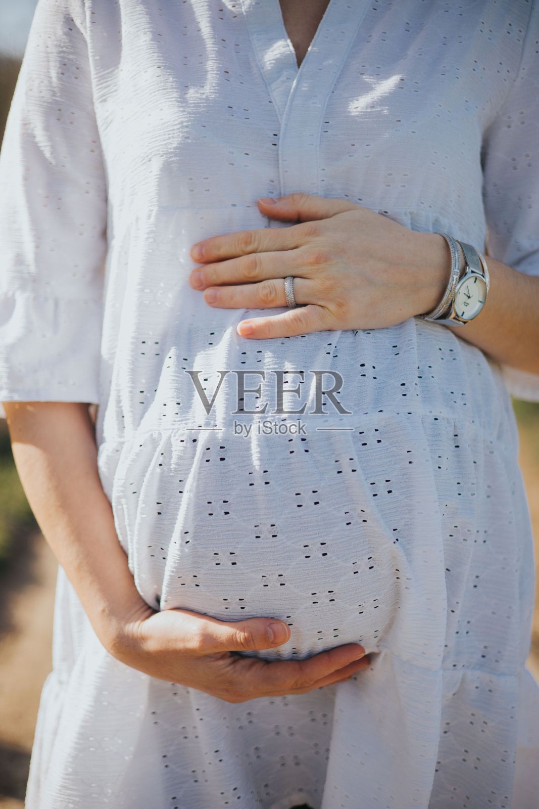 年轻的孕妇穿着白色的裙子,在公园里捂着肚子照片摄影图片