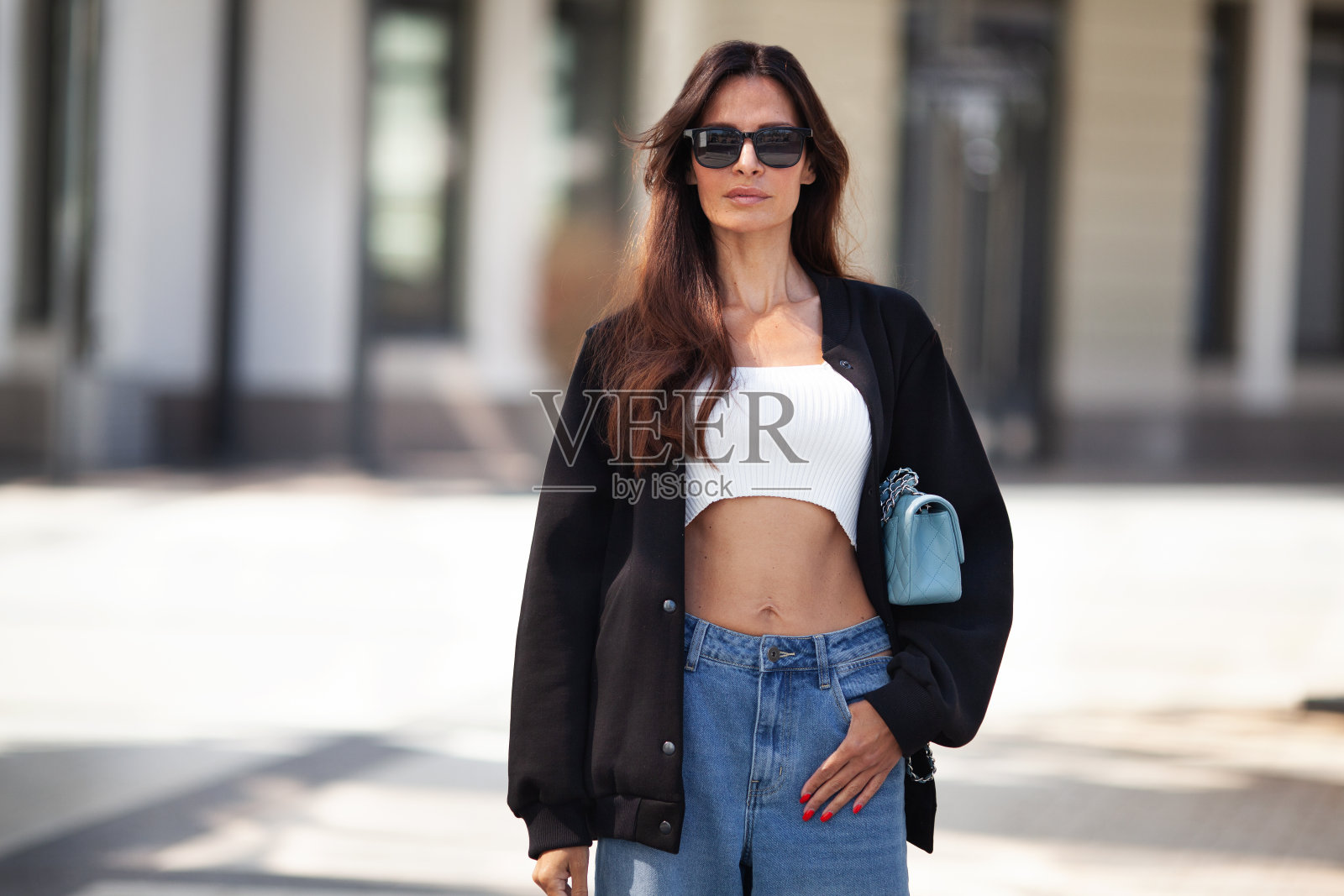 美丽时尚的黑发女人站在城市街道的肖像。时尚女模特穿着黑色飞行员夹克,露肚子,牛仔裤,太阳镜。街头风格照片摄影图片