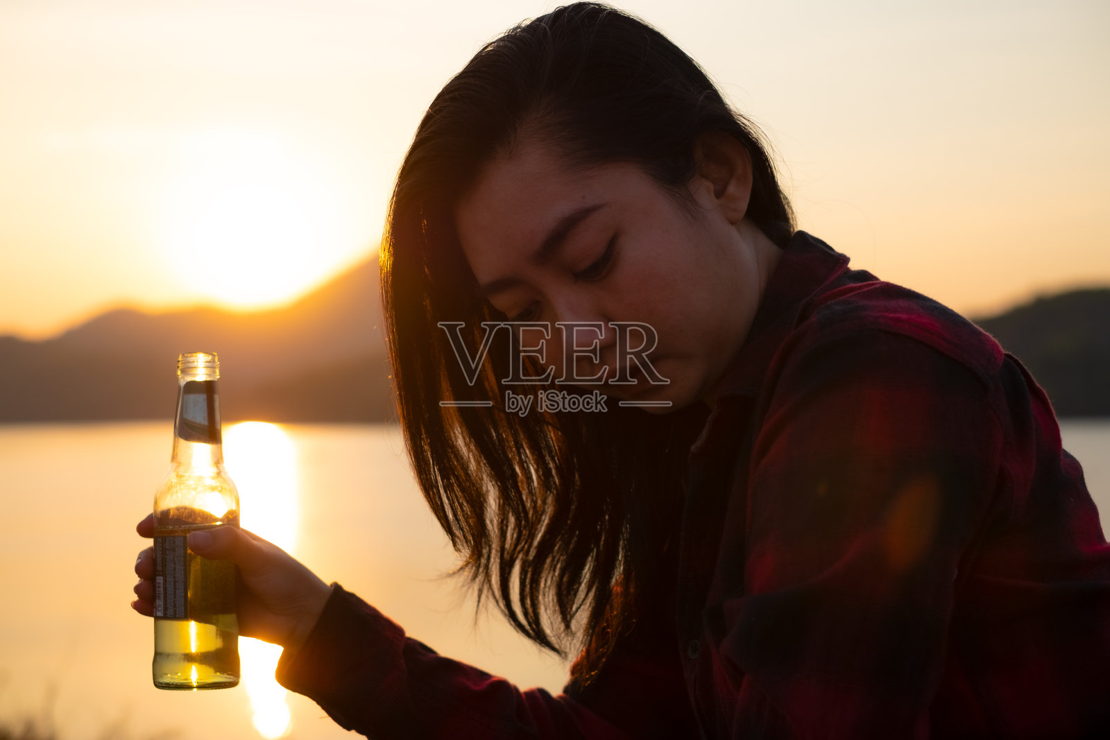 夕阳下沙滩上一个手持啤酒瓶的女人的剪影照片摄影图片