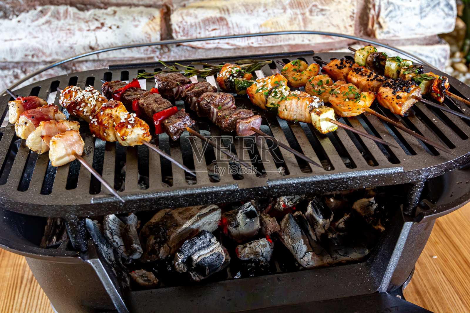 很多肉、鱼、鸡、虾、蔬菜串在木头串上,放在一个小铸铁烤架上煎照片摄影图片