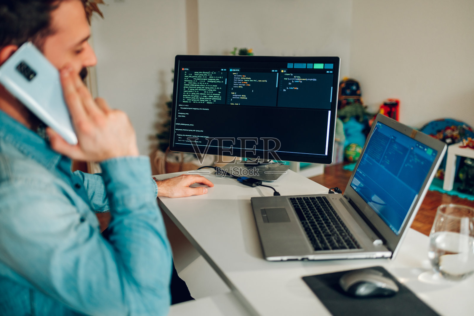 一位高级开发人员坐在他的家庭办公室里接电话。选择性地关注他电脑上的代码。照片摄影图片