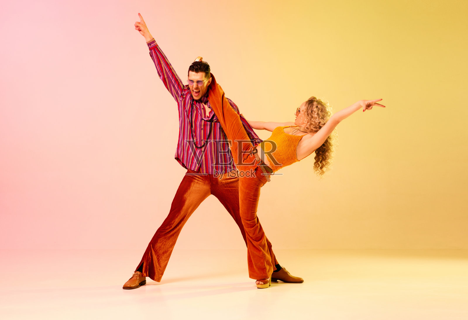 艺术,才华横溢,感性的年轻人,男人和女人穿着时尚的衣服,在渐变的粉黄色背景下跳迪斯科舞照片摄影图片