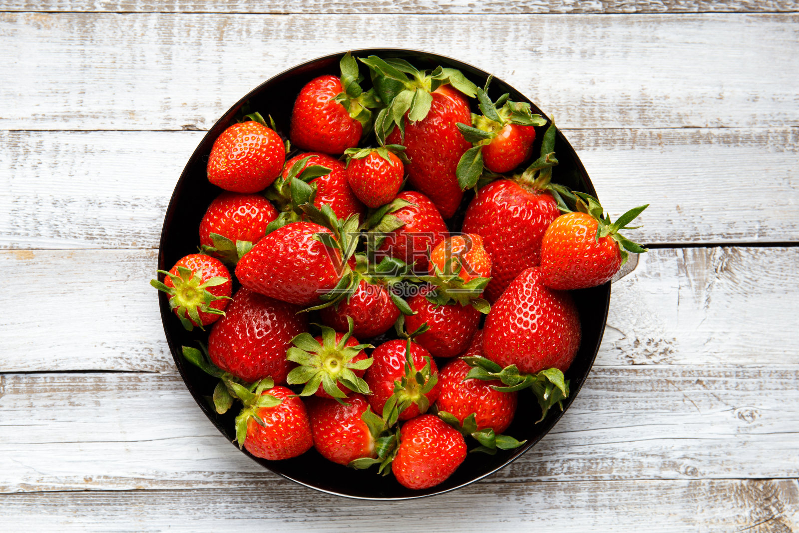 新鲜的有机草莓在一个黑色的圆形盘子上,浅色的木制背景,俯视图。照片摄影图片