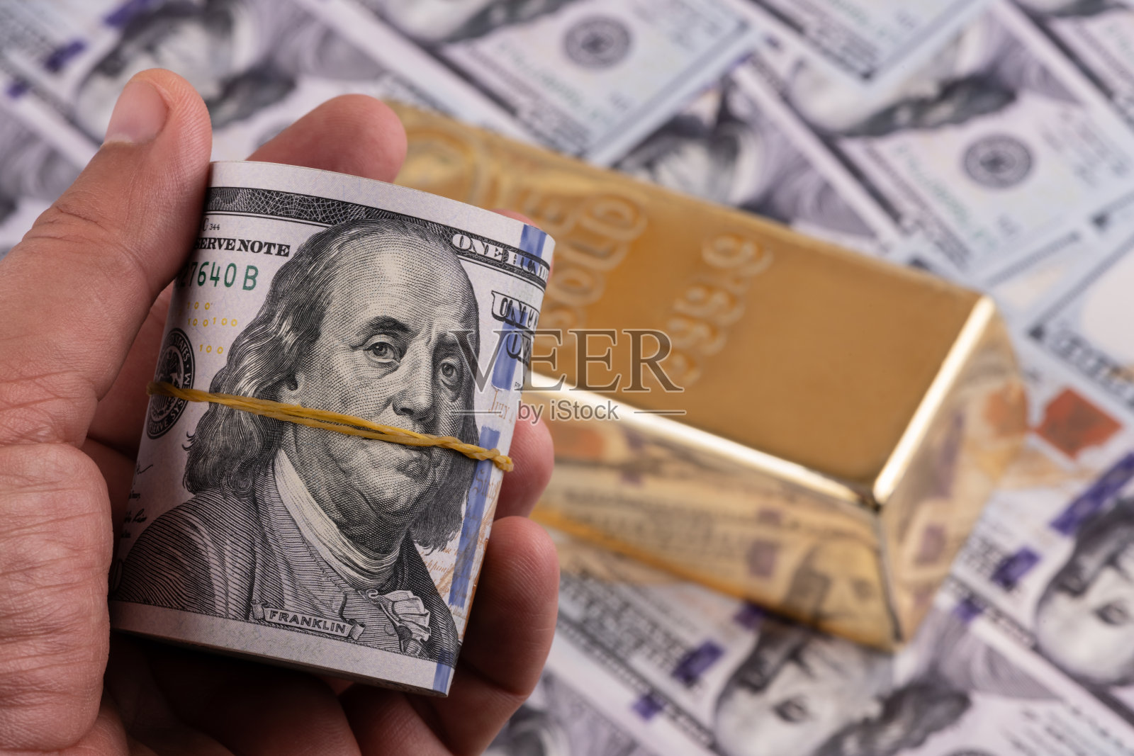 一个男人手里拿着一叠100美元钞票和一根金条照片摄影图片