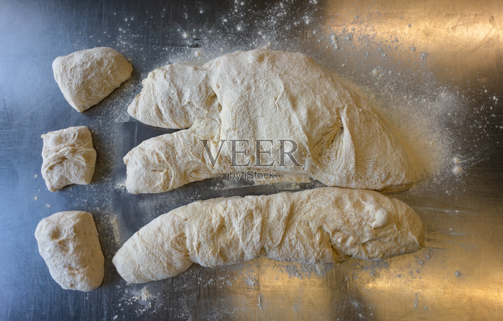 在金属桌子上用工作台刮刀切恰巴塔面团俯视图照片摄影图片