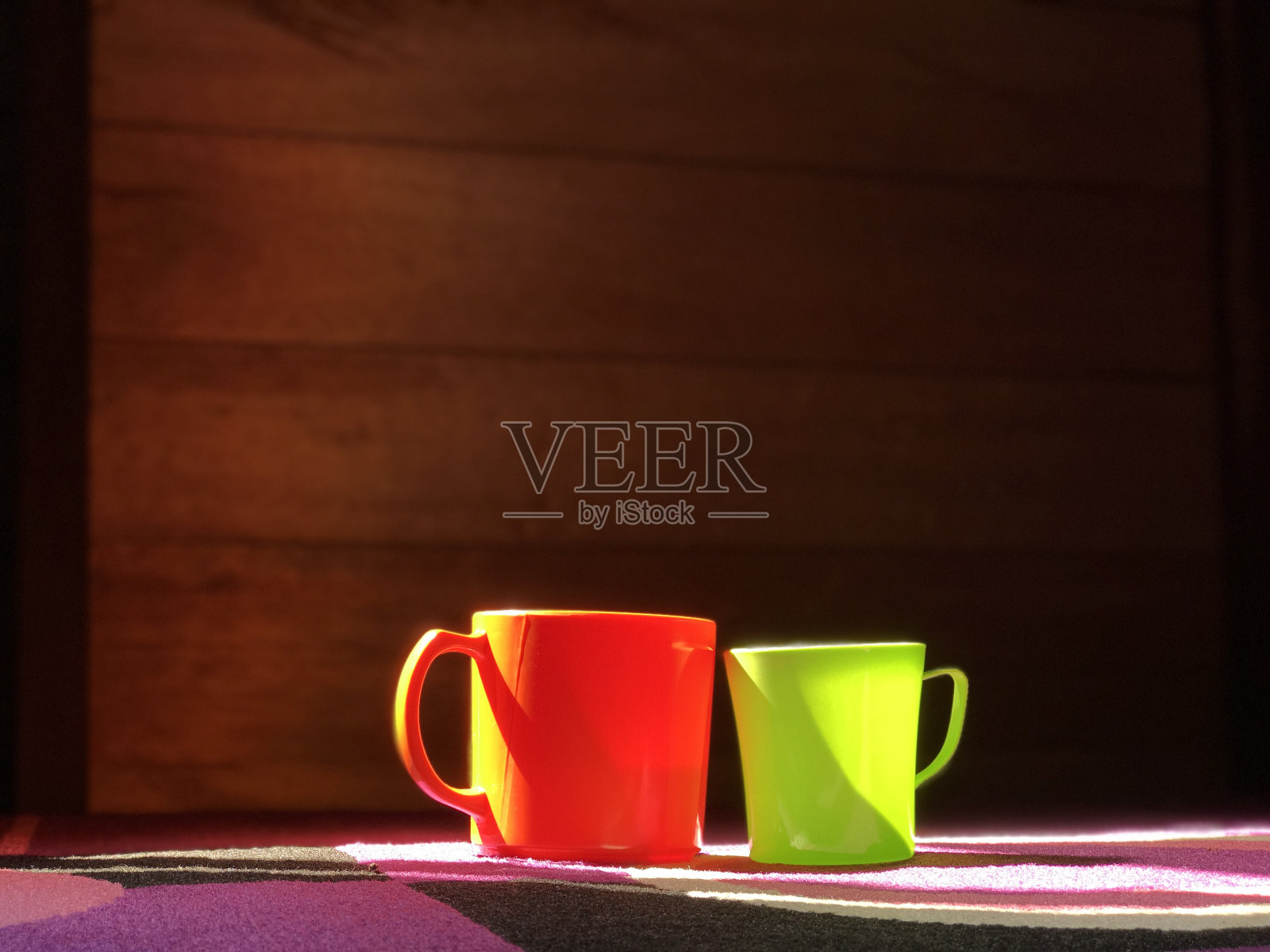 杯子是橙色和绿色,地毯是紫色的。漂亮的杯子照片摄影图片