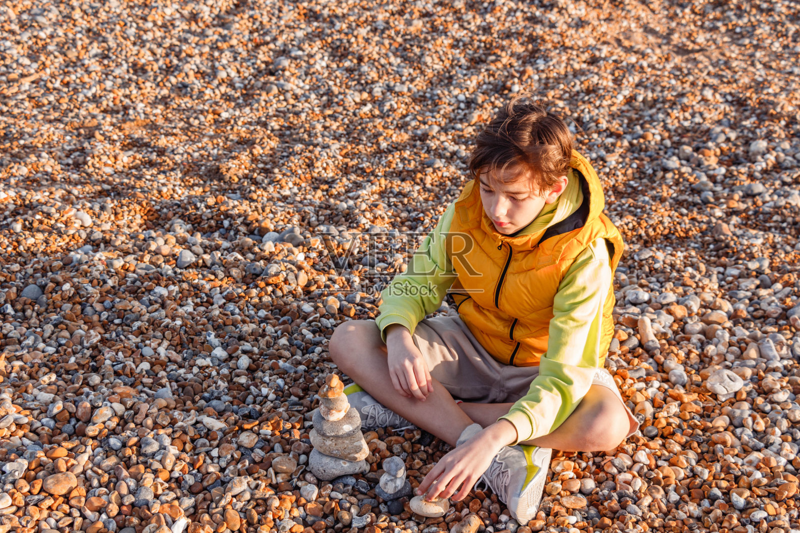 俯视图,一个男孩坐在卵石沙滩上,手里拿着一堆石头照片摄影图片