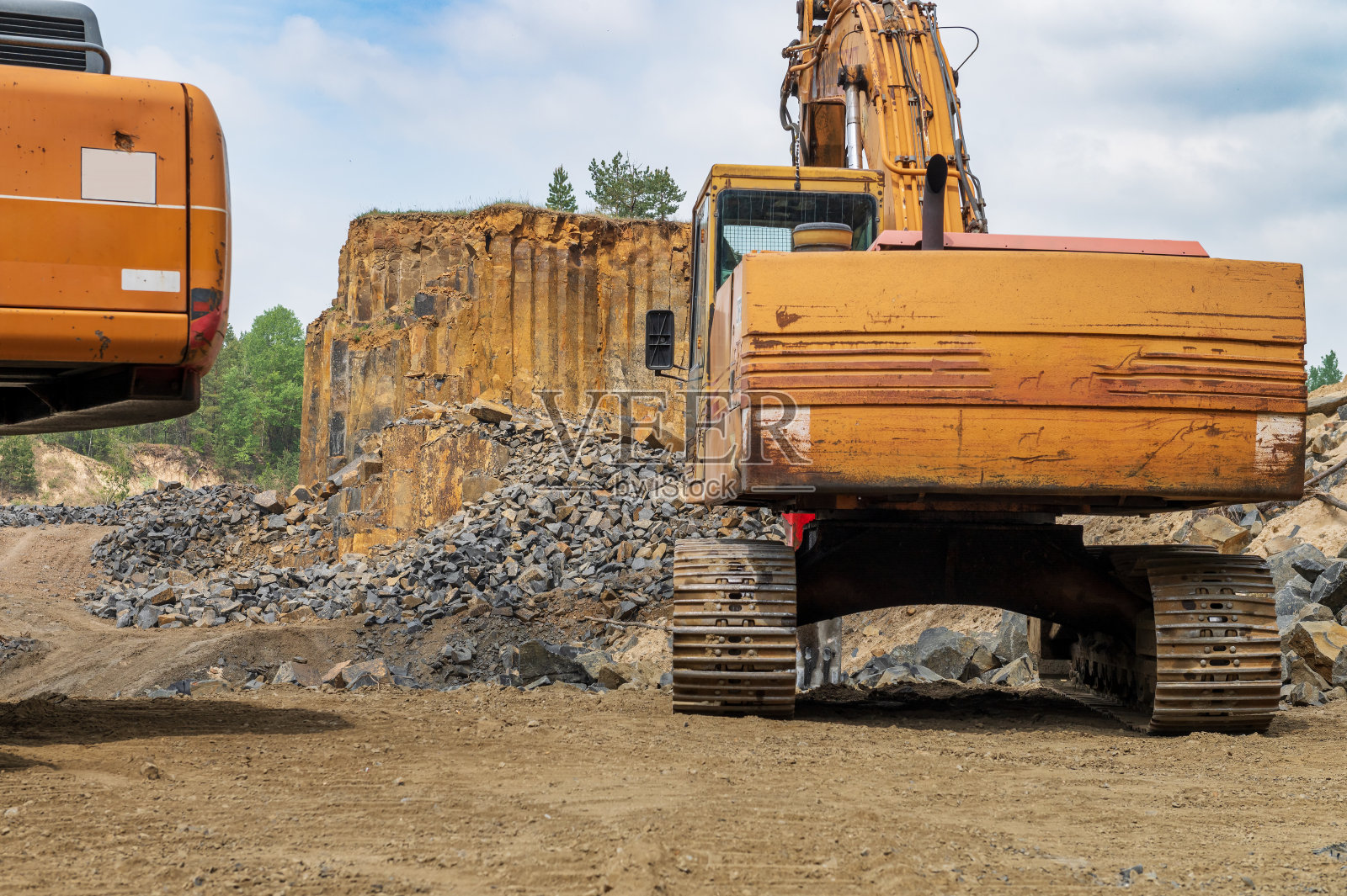 玄武岩挖掘。森林附近玄武岩采石场的黄色挖掘机。露天矿山中的大型橙色挖掘机照片摄影图片