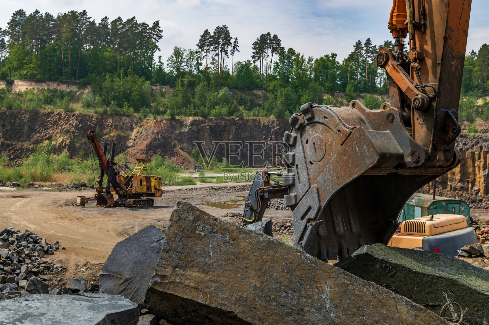 玄武岩挖掘。森林附近玄武岩采石场的黄色挖掘机。露天矿山中的大型橙色挖掘机照片摄影图片