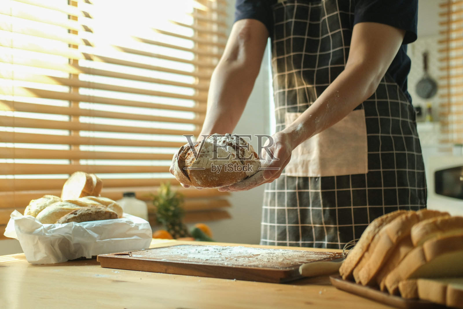 在明亮的厨房里,戴着围裙的男面包师手拿着一个酸面包。照片摄影图片