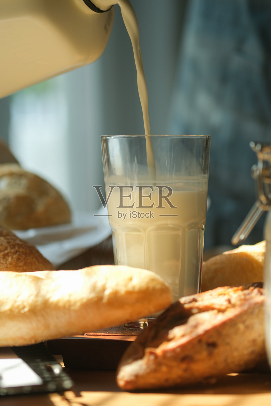 在厨房准备早餐的男子往玻璃杯里倒牛奶的特写镜头。照片摄影图片