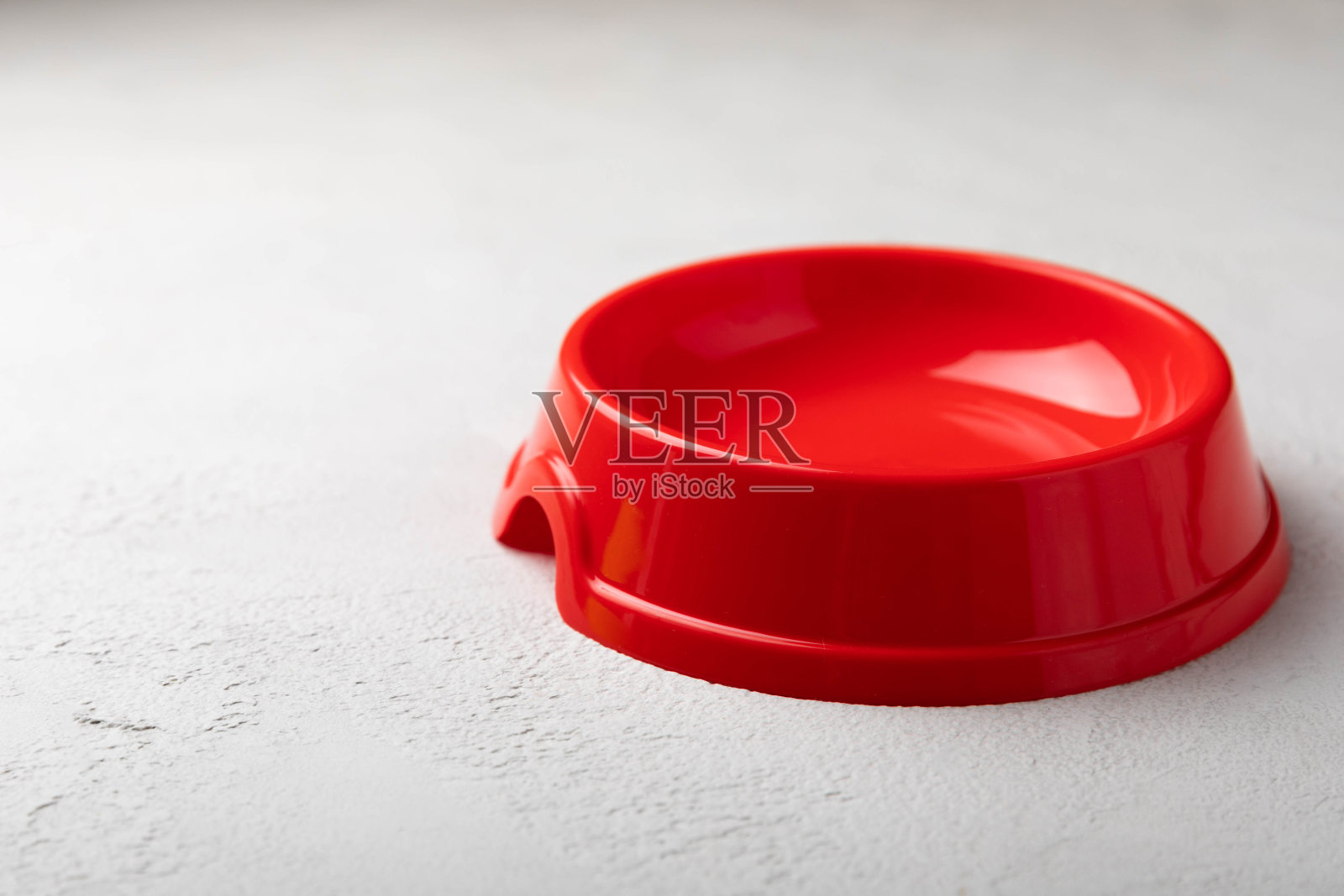 水泥背景上喂猫狗的红色碗。为宠物提供健康和能量的维生素和营养素。副本的空间。照片摄影图片