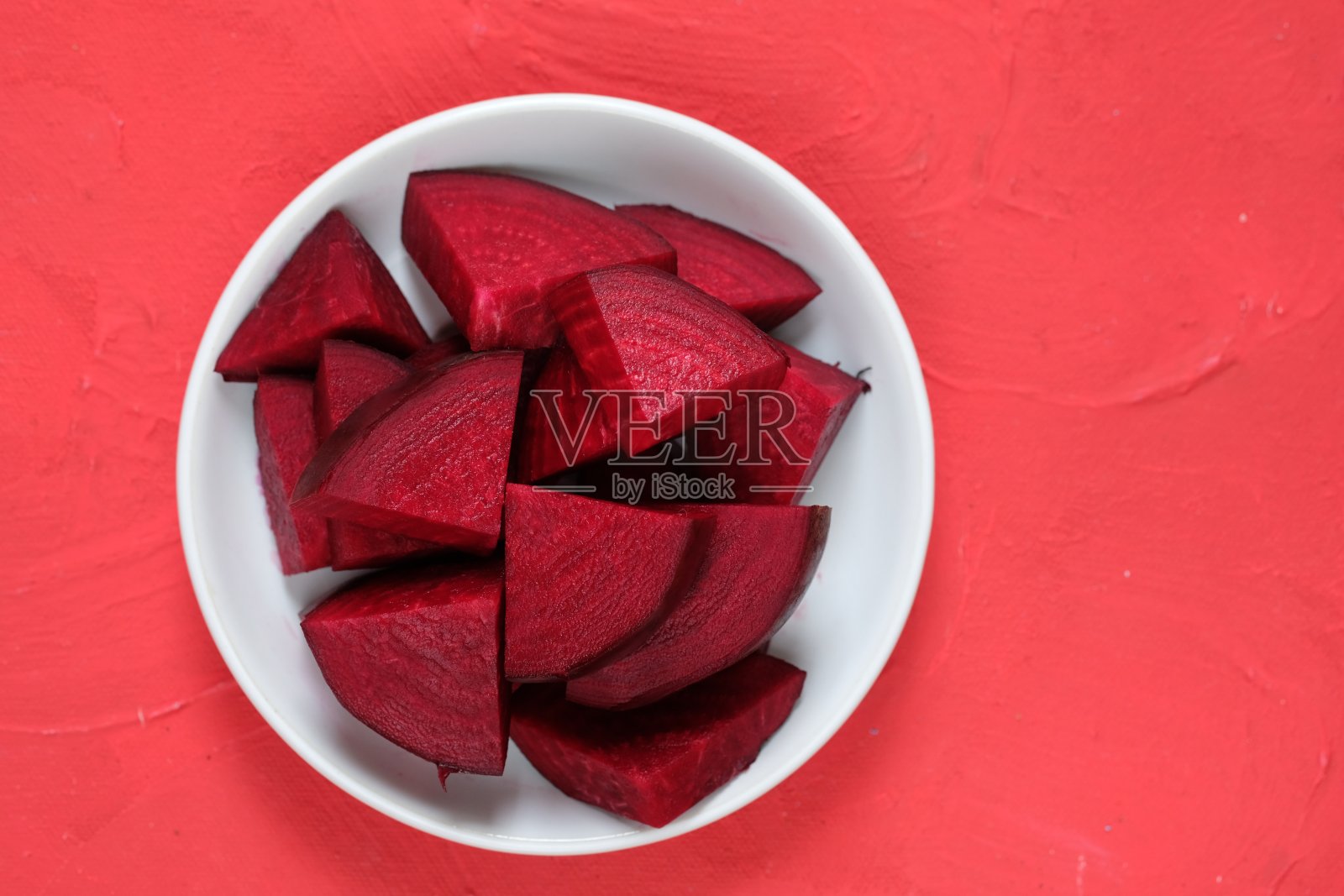 β寻常的。切好的甜菜根放在红色桌子上的白色盘子里。金色甜菜或红色甜菜。红色蔬菜。照片摄影图片
