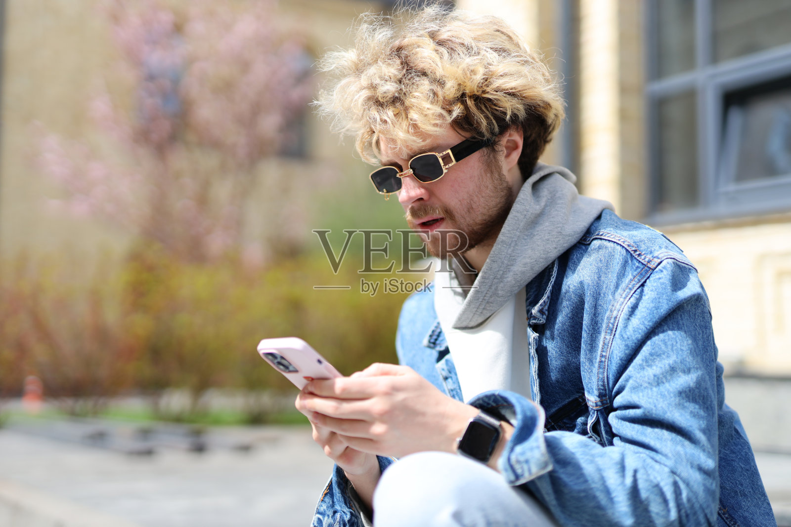 一个时髦的现代男人坐在外面,手里拿着智能手机。照片摄影图片