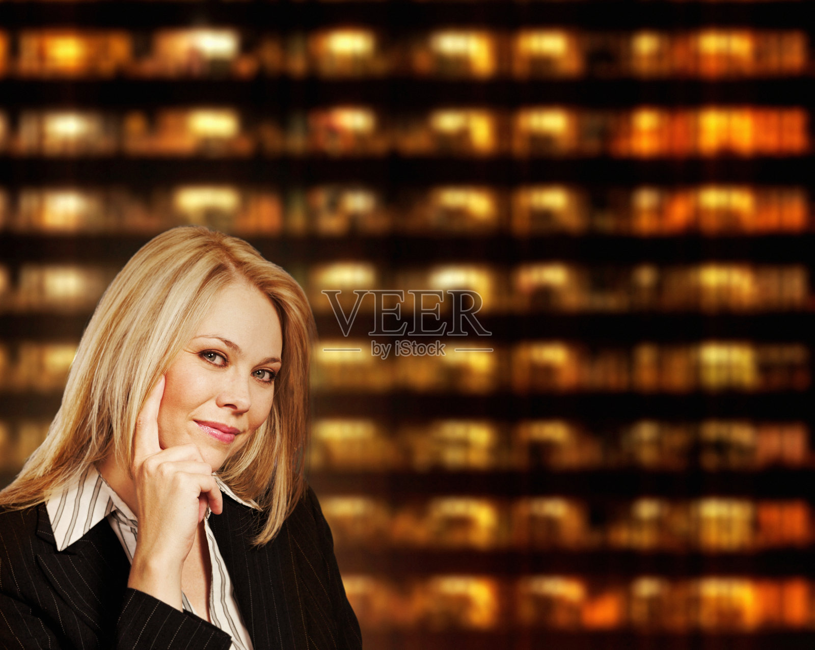 美丽的年轻金发女郎在一幢灯火辉煌的建筑物的夜晚背景下,给了镜头一种快乐或可能是调情的表情照片摄影图片