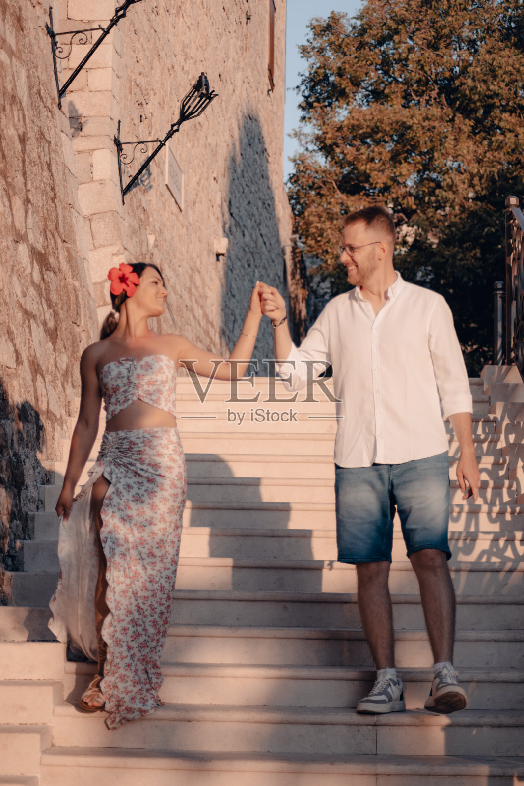 年轻的夫妇走下楼梯,手牵着手,看着对方,微笑着照片摄影图片