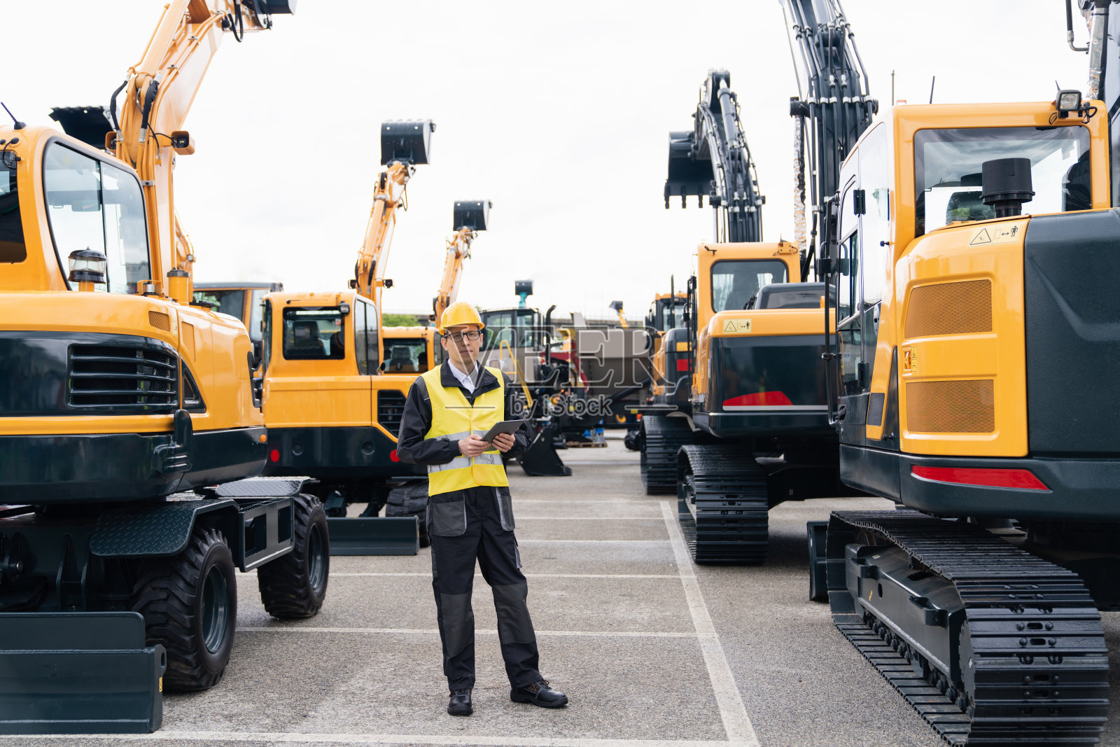 工程师戴着头盔,在建筑挖掘机旁放着一个数字平板电脑照片摄影图片