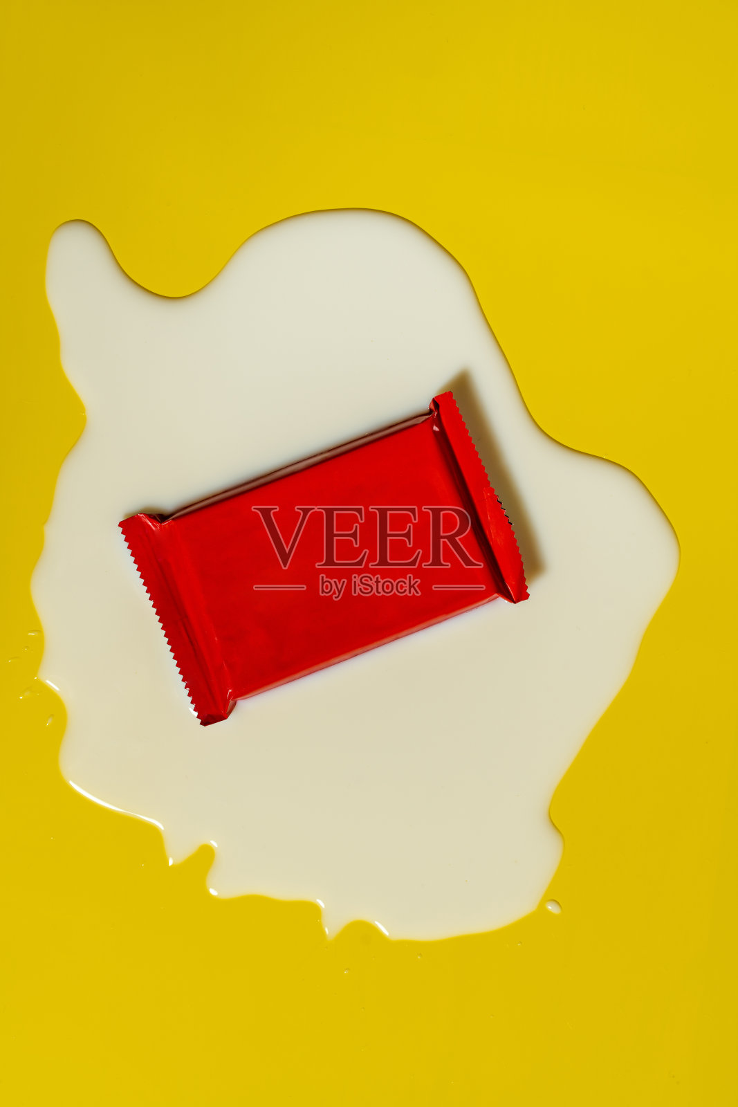 空白红色包装的一块巧克力威化饼在一滩洒出的牛奶中照片摄影图片