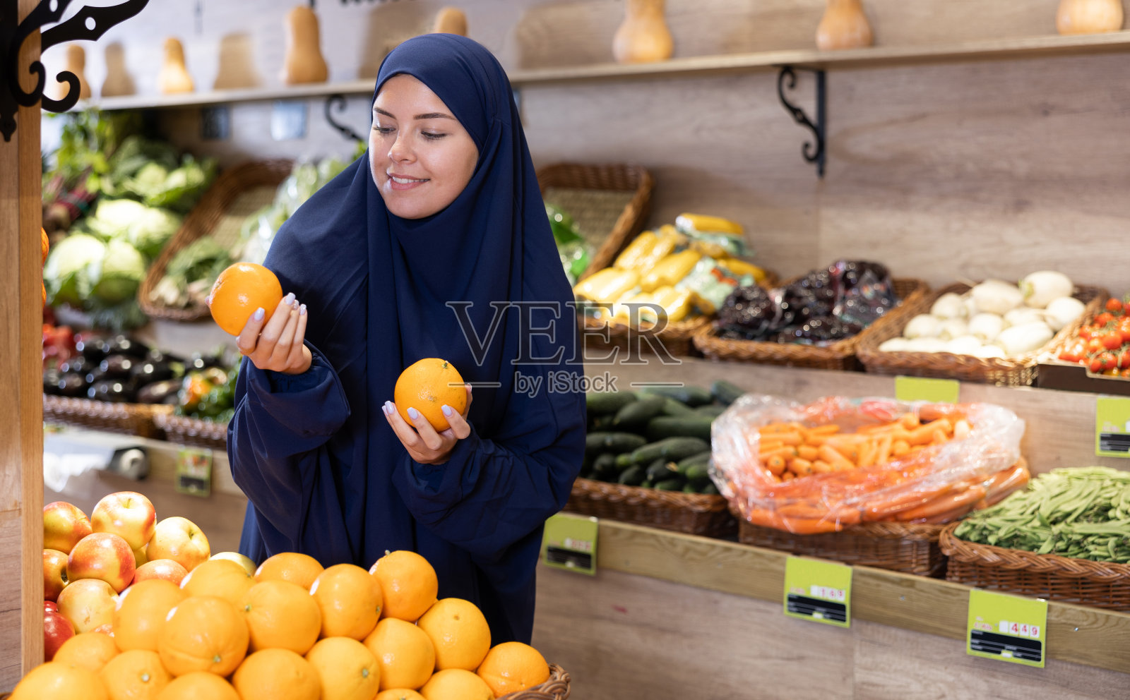 高兴的年轻穆斯林妇女在杂货店挑选橙子照片摄影图片