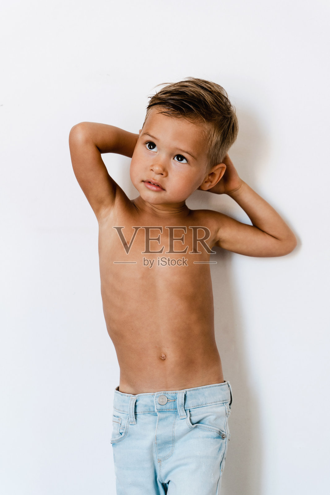 可爱的小男孩穿着蓝色牛仔裤,像时尚模特一样在白色背景下摆姿势照片摄影图片