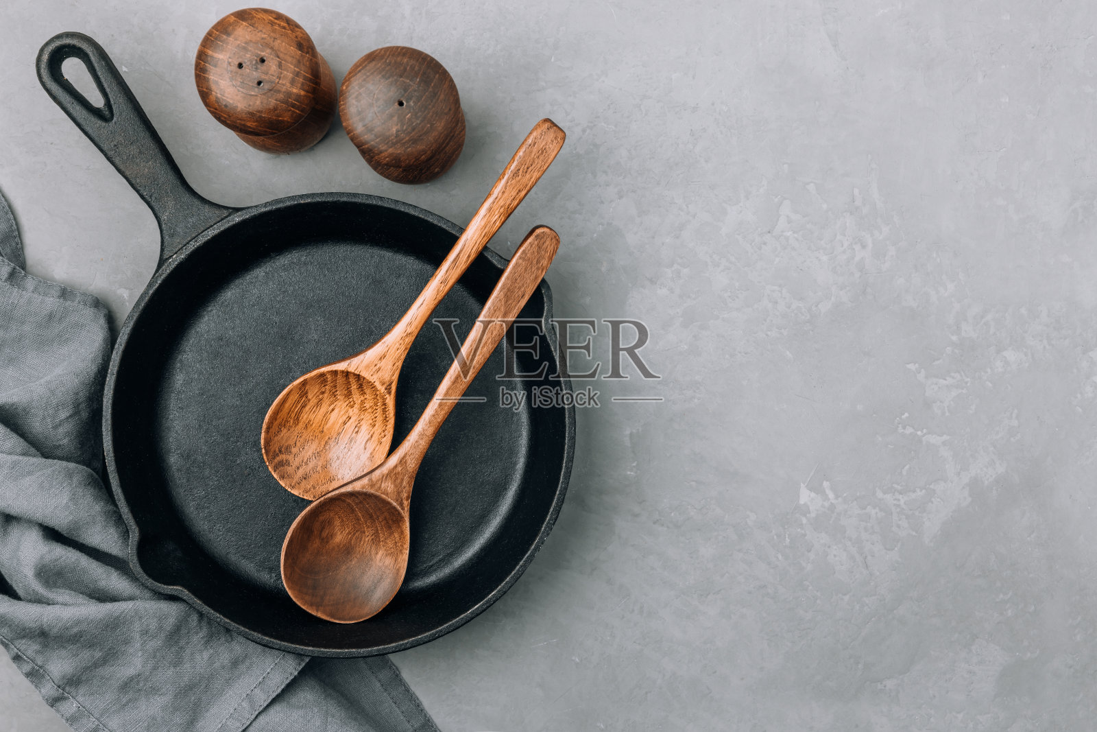 空盘。灰色石头背景上的铸铁平底锅和木制勺子,俯视图,复制空间。照片摄影图片