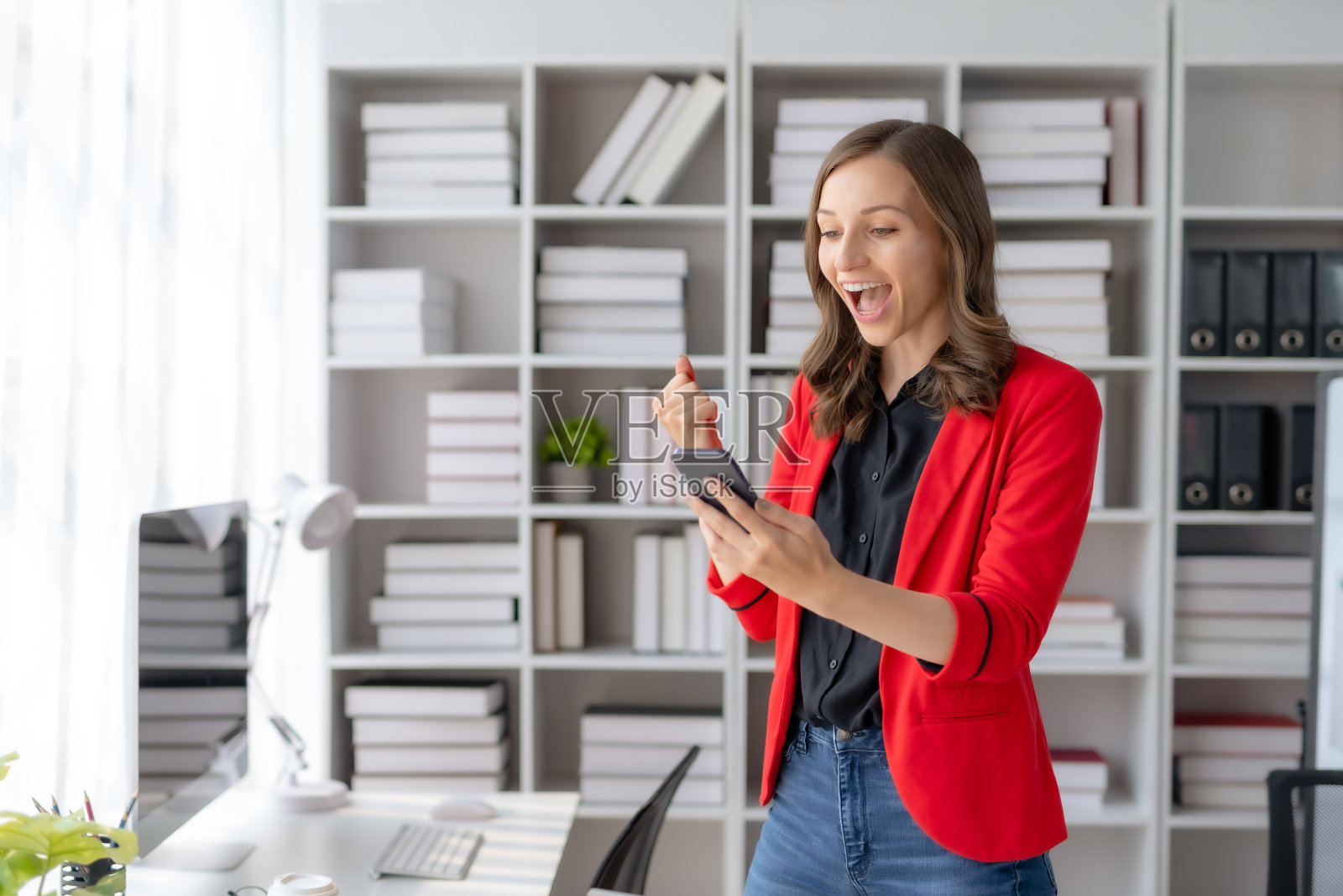 快乐的女商人举起胜利的手,拿着智能手机开心地微笑。工作中成功的概念。照片摄影图片