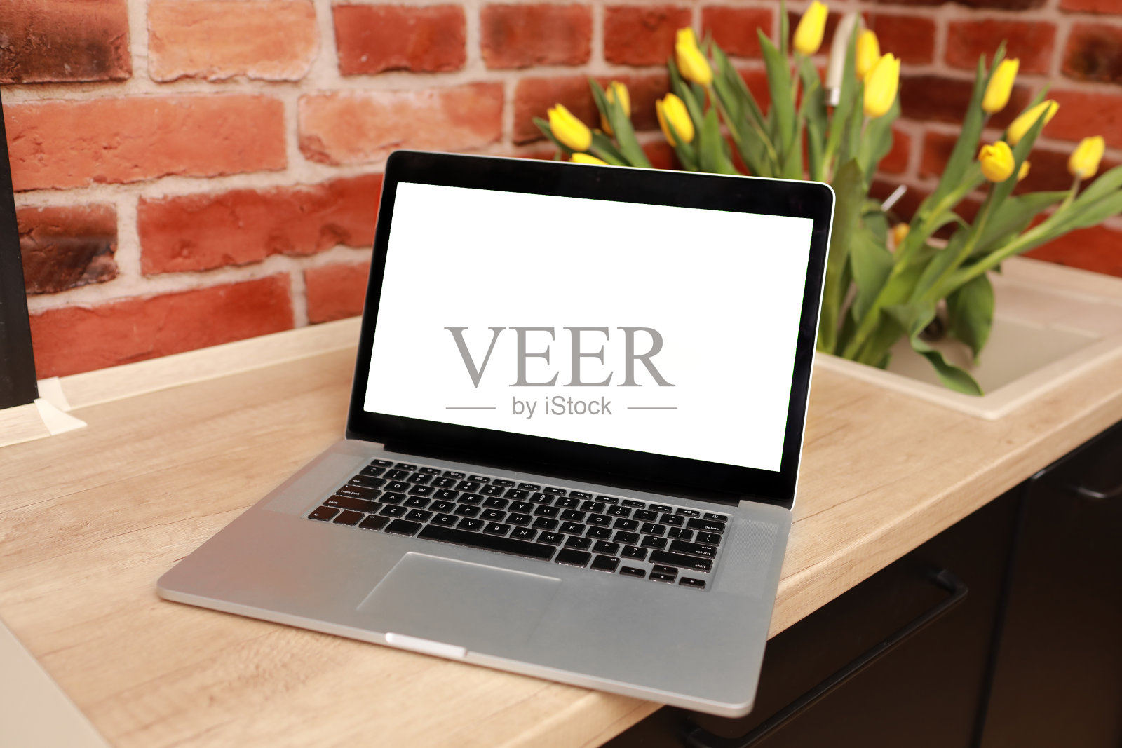 商业,自由职业者,博客的概念。在家庭办公室里,木桌上的笔记本电脑上有空白的白色屏幕,砖墙旁,花瓶里插着黄色的郁金香。模拟,复制空间。社交媒体,网站模板照片摄影图片
