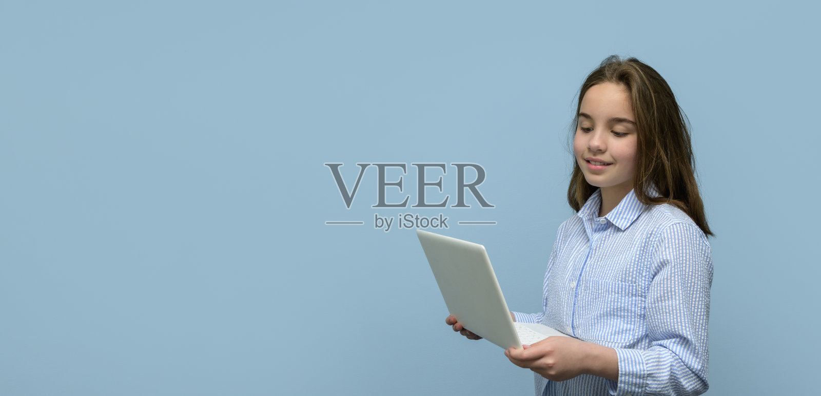 一个拿着蓝色背景白色笔记本电脑的女孩。横幅照片摄影图片