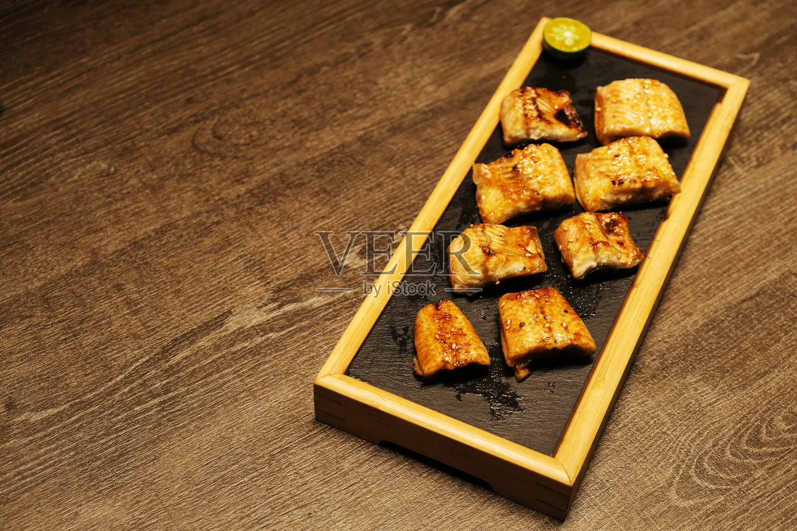 切成薄片的烤鳗鱼肉放在盘子里,放在桌子上照片摄影图片