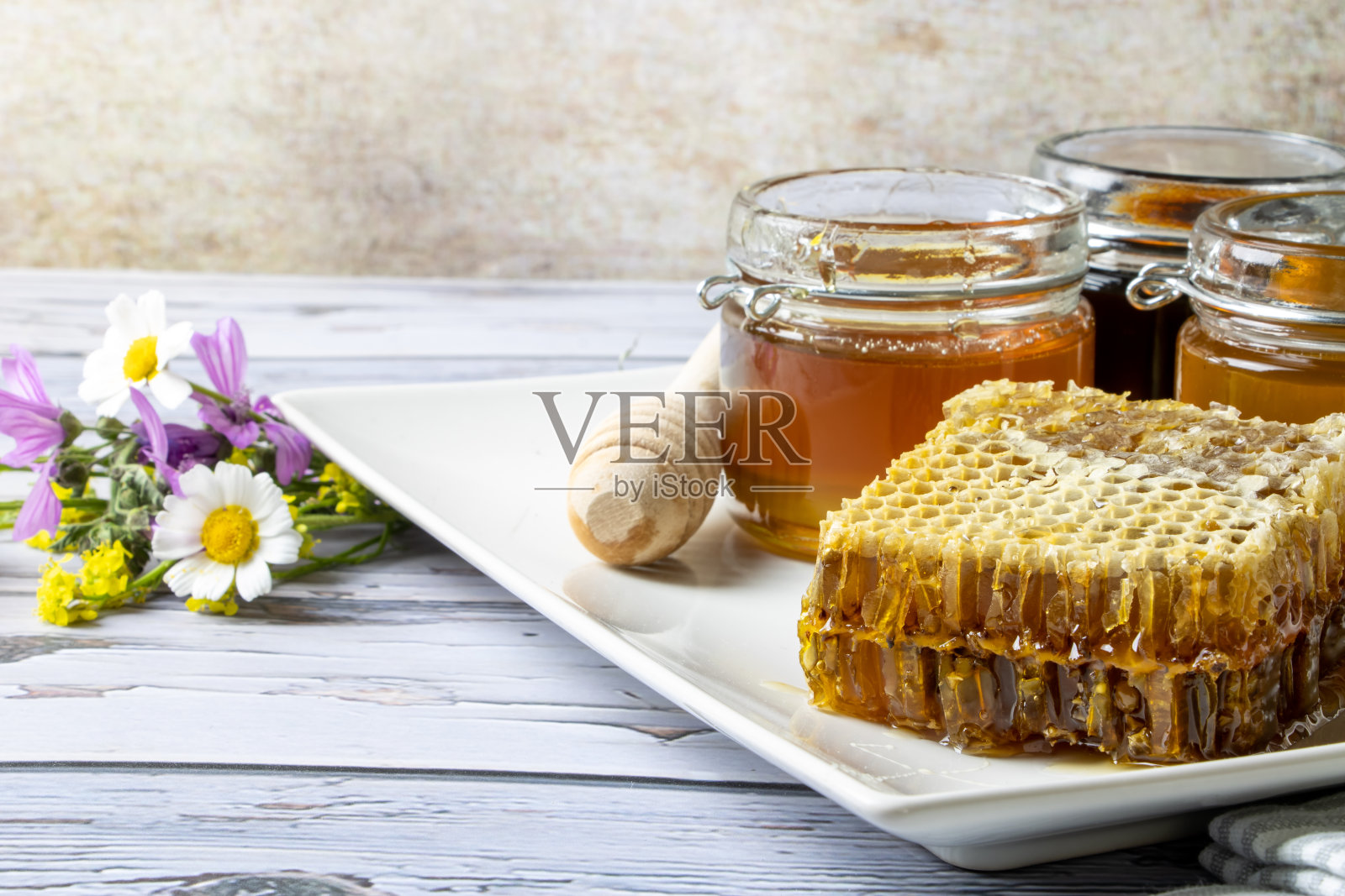 装有不同种类蜂蜜的罐子,旁边是蜂巢,还有一个盛着野花的盘子上的蜂蜜勺照片摄影图片