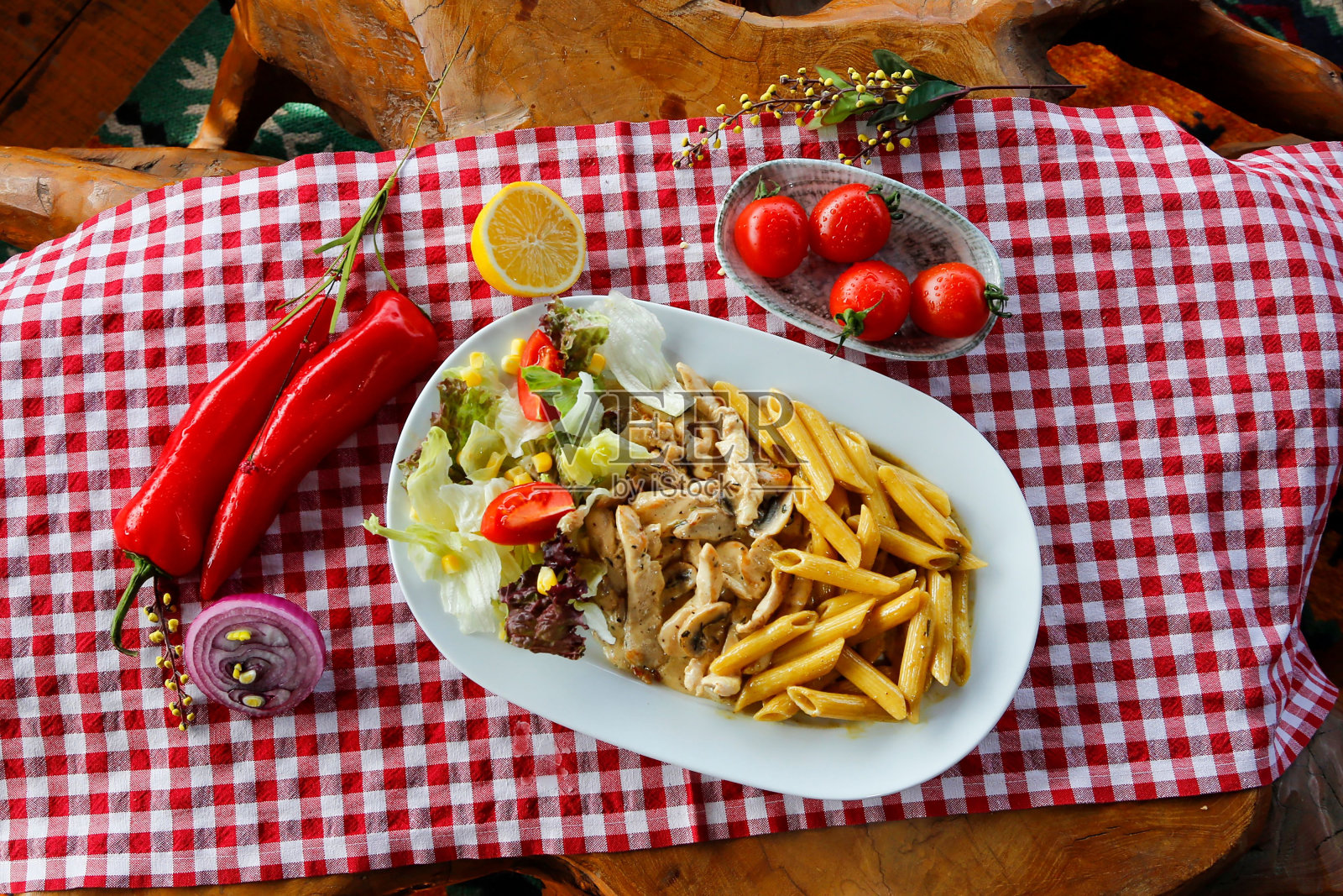 一盘开胃的意大利通心粉,配上鸡肉、沙拉和其他蔬菜,铺在格子桌布上照片摄影图片