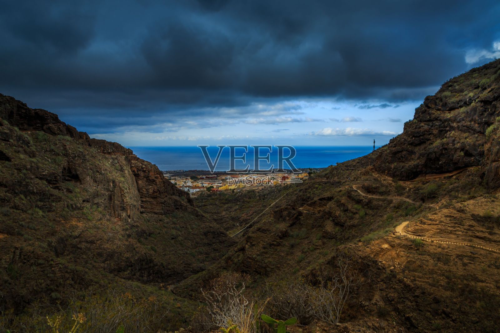 海岸上的小住宅区可以透过崎岖的山脉看到,上面有戏剧性的云照片摄影图片