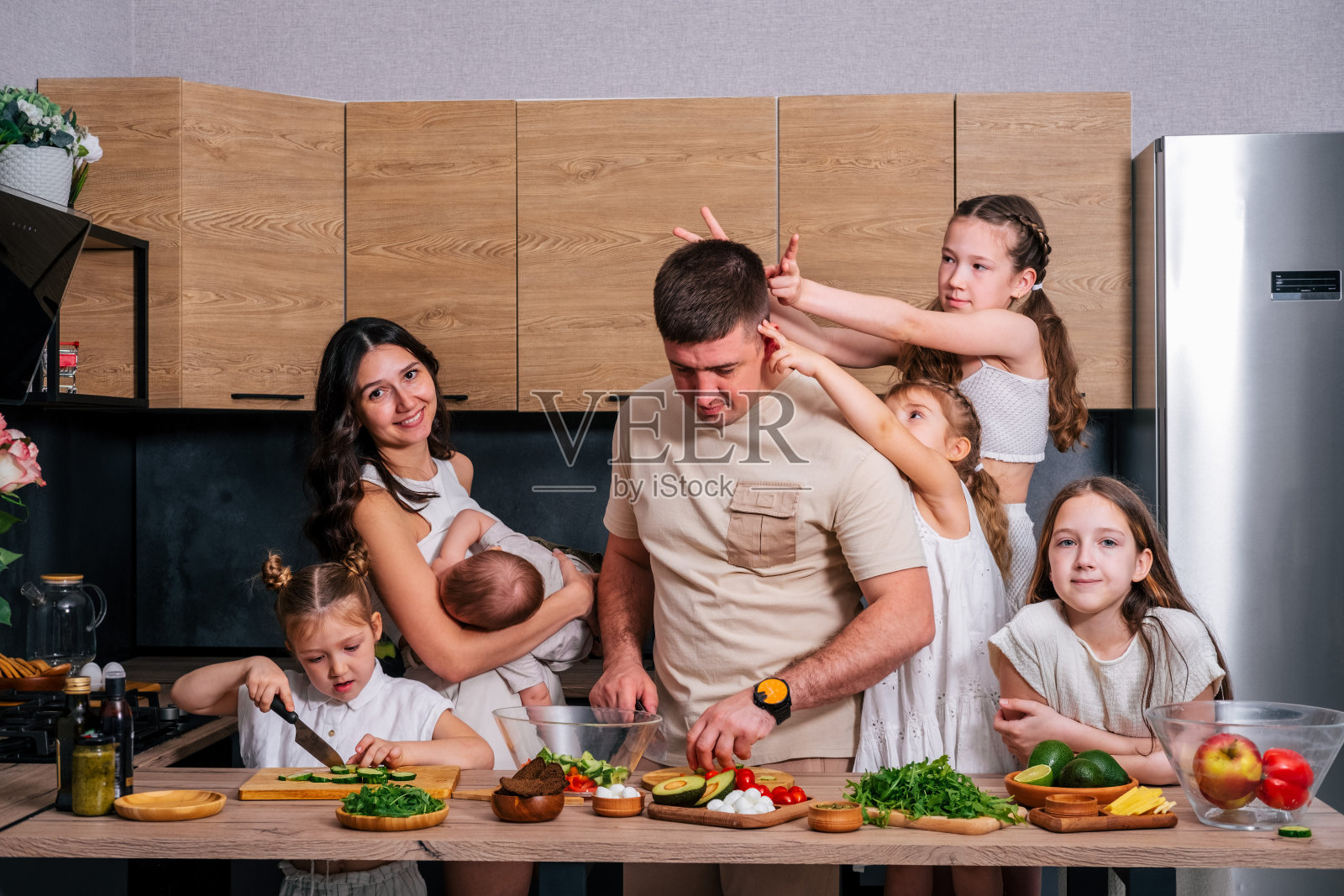 一个大家庭——妈妈、爸爸、4个女儿和一个儿子在一个现代化的厨房里一起准备午餐沙拉。大家庭在一起的概念。照片摄影图片