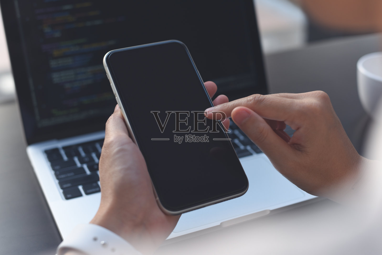 办公室桌子上的笔记本电脑上工作时,女性手使用空白屏幕手机的模拟图像照片摄影图片