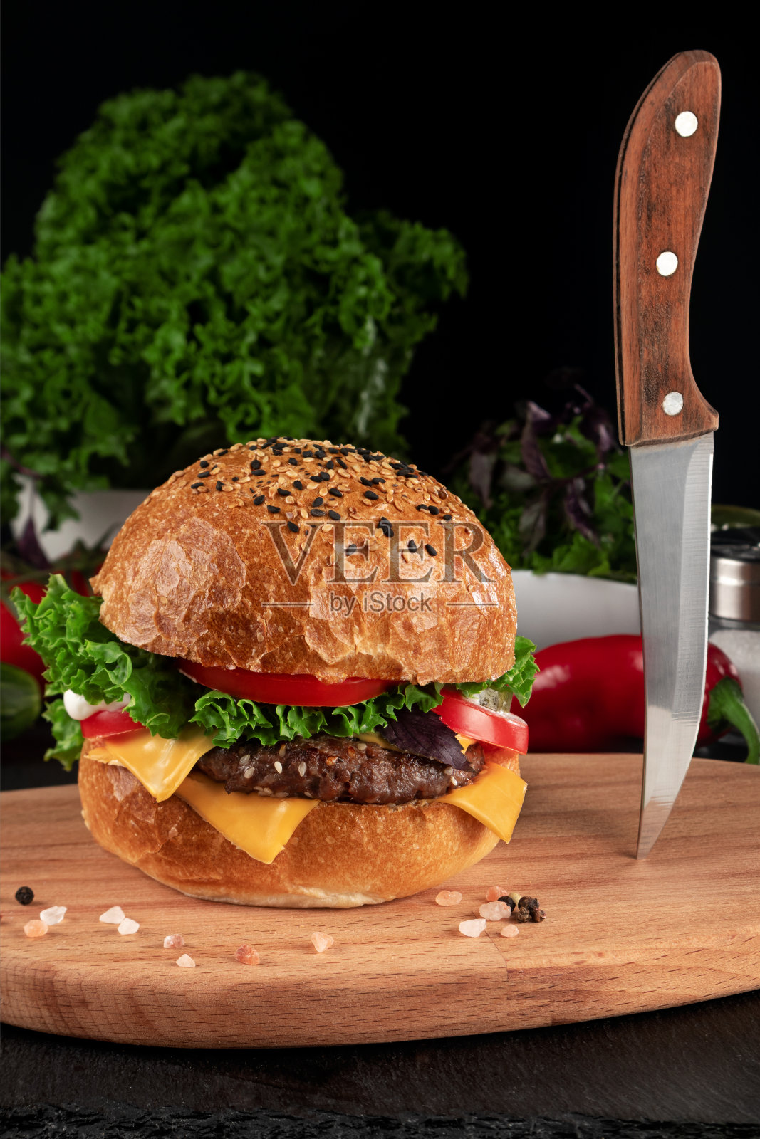 汉堡放在砧板上,黑色背景上有一把刀。照片摄影图片
