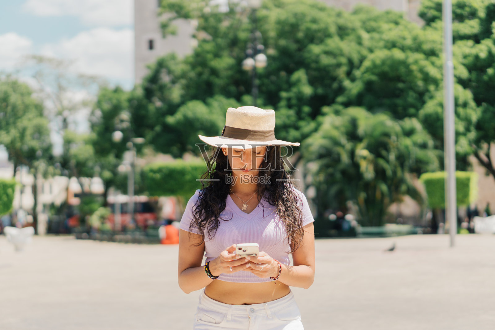 一个女人在阳光明媚的日子里走在街上,一边用手机发短信。照片摄影图片